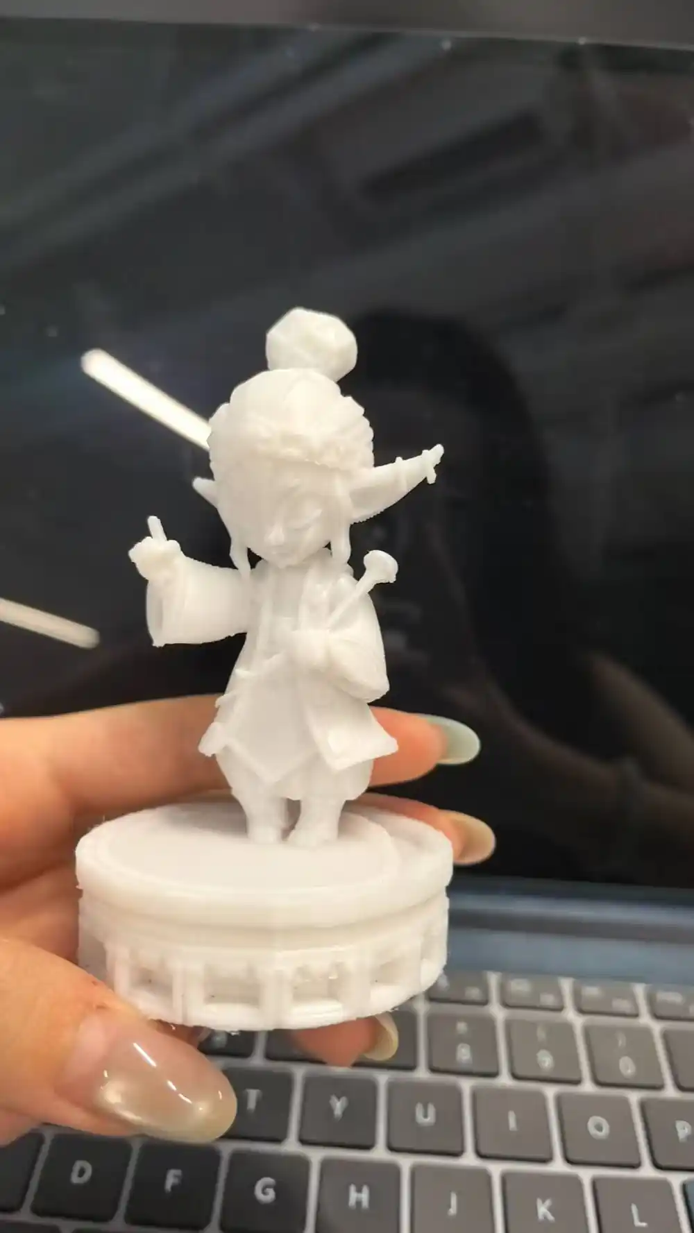 手持未上色的小绿茶白模，背后是制作工作台